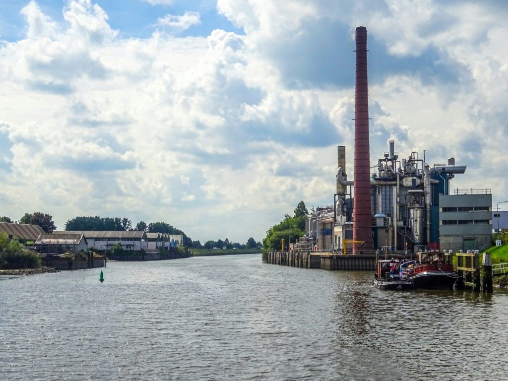 Industrieanlage mit hohem Schornstein neben einem Fluss.